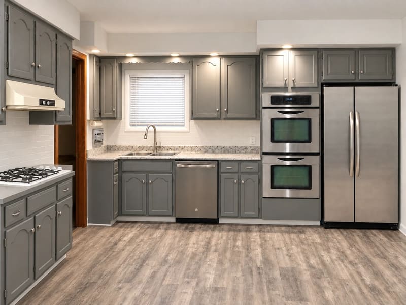 A renovated kitchen with gray cabinets, white tile backsplash, a cooktop and wood-look flooring