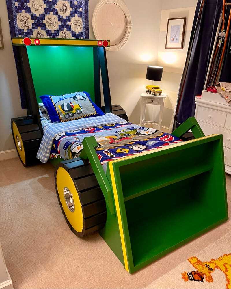 A finished custom green tractor bed with yellow wheels and a front loader shelf in a child's room