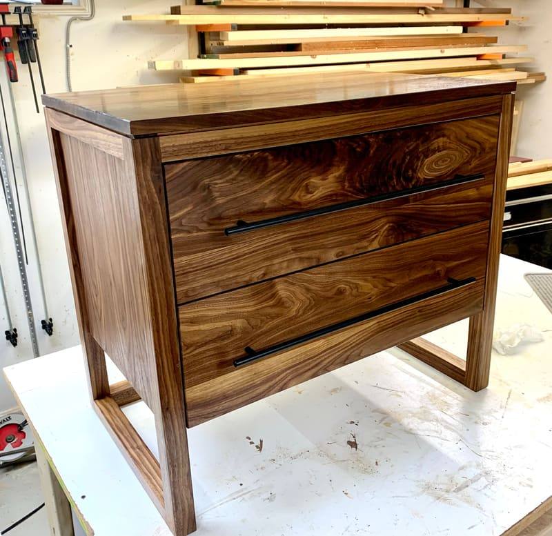 A two-drawer walnut dresser with black bar pulls and richly figured drawer fronts