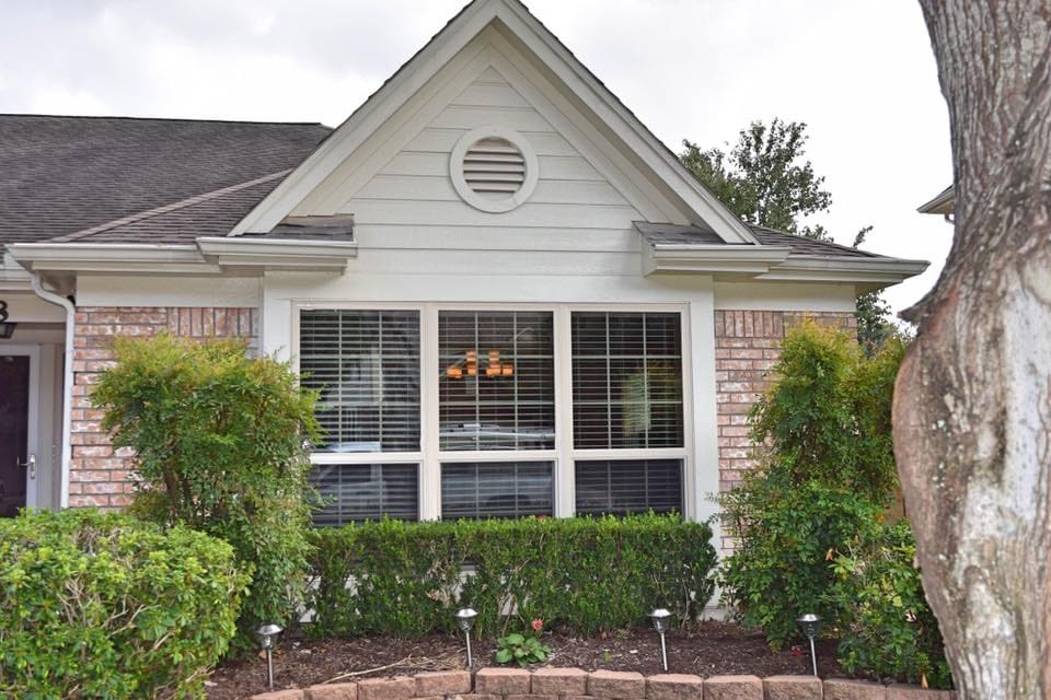 Large three-part window with blinds on the front of a brick house, a project by Symphony Home Improvement.