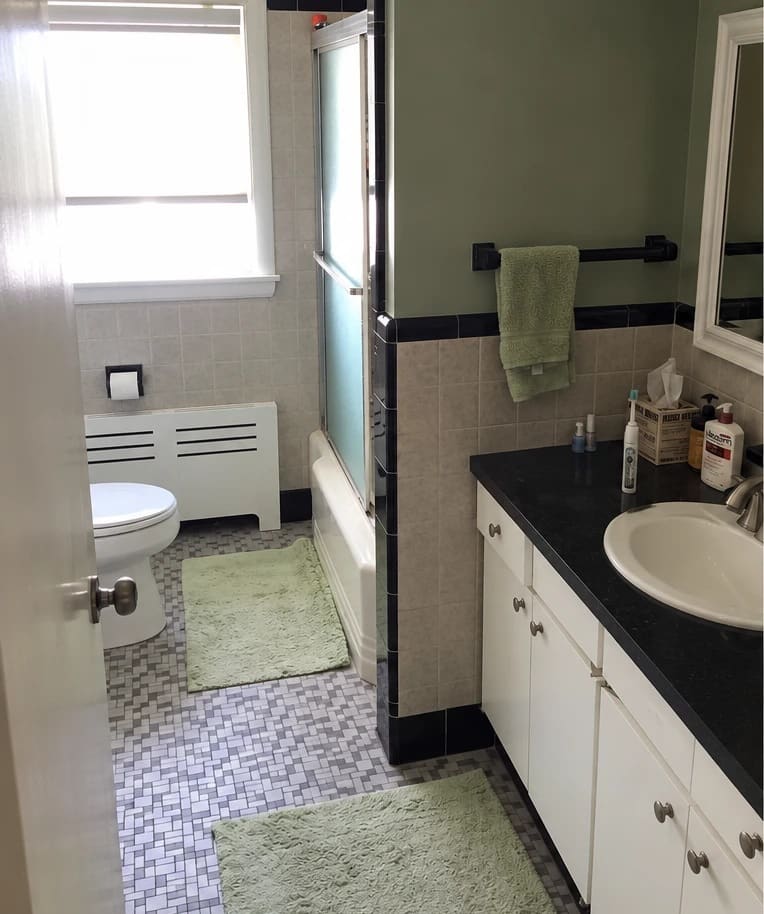 Bathroom before the update, with green walls, beige wall tile with a black border, a mosaic floor and a dark countertop