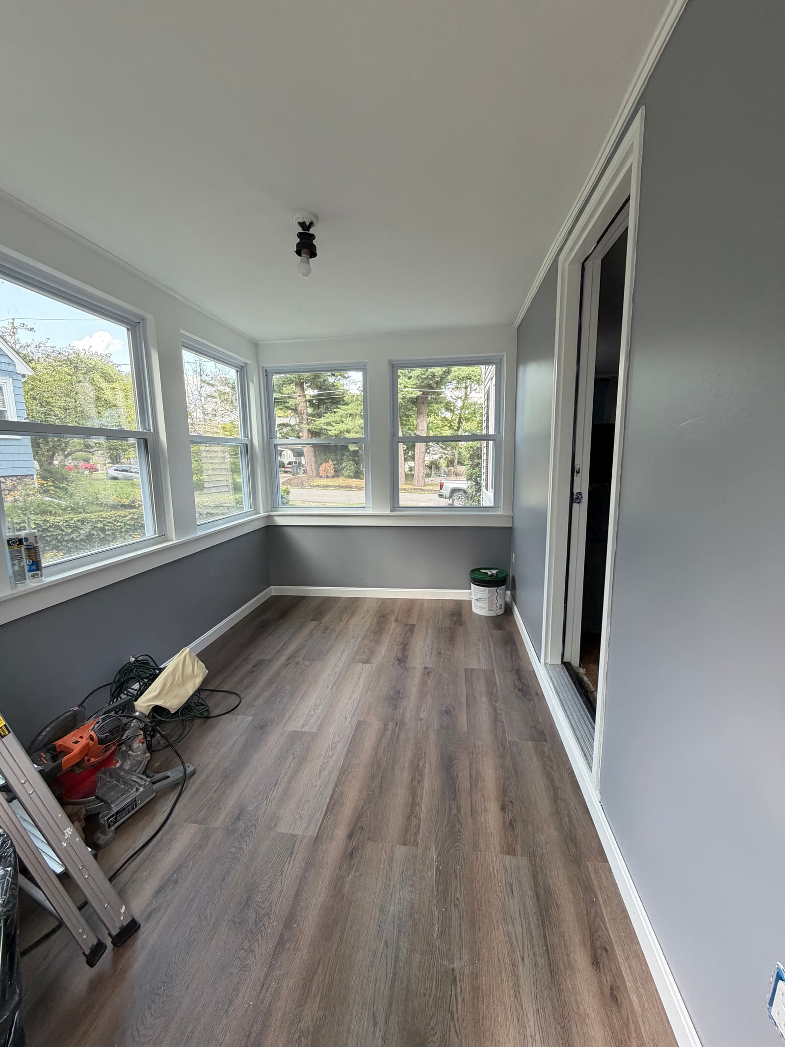 The same sunroom after the work, with painted gray walls and new plank flooring