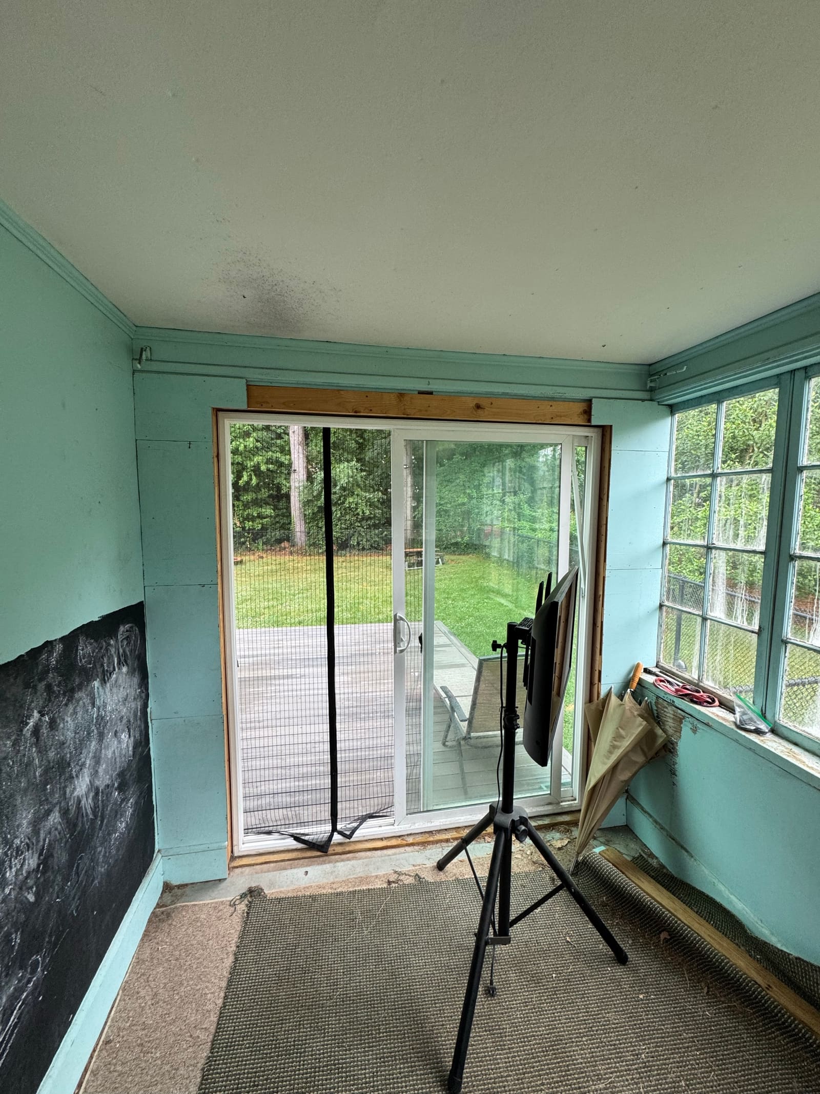 A dated green sunroom before the renovation, with a sliding door, worn walls and a worn floor