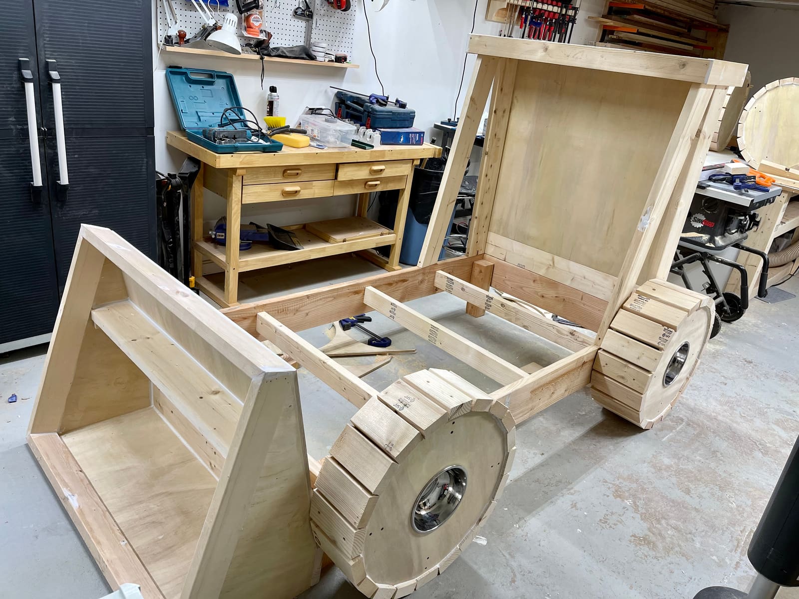 A custom child's tractor bed frame under construction in the shop, with raw wood and big slatted wheels