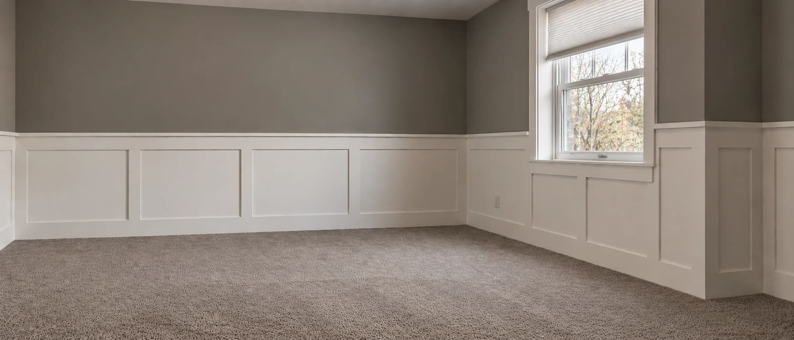A bedroom with white shaker-style wainscoting panels and chair rail below gray walls