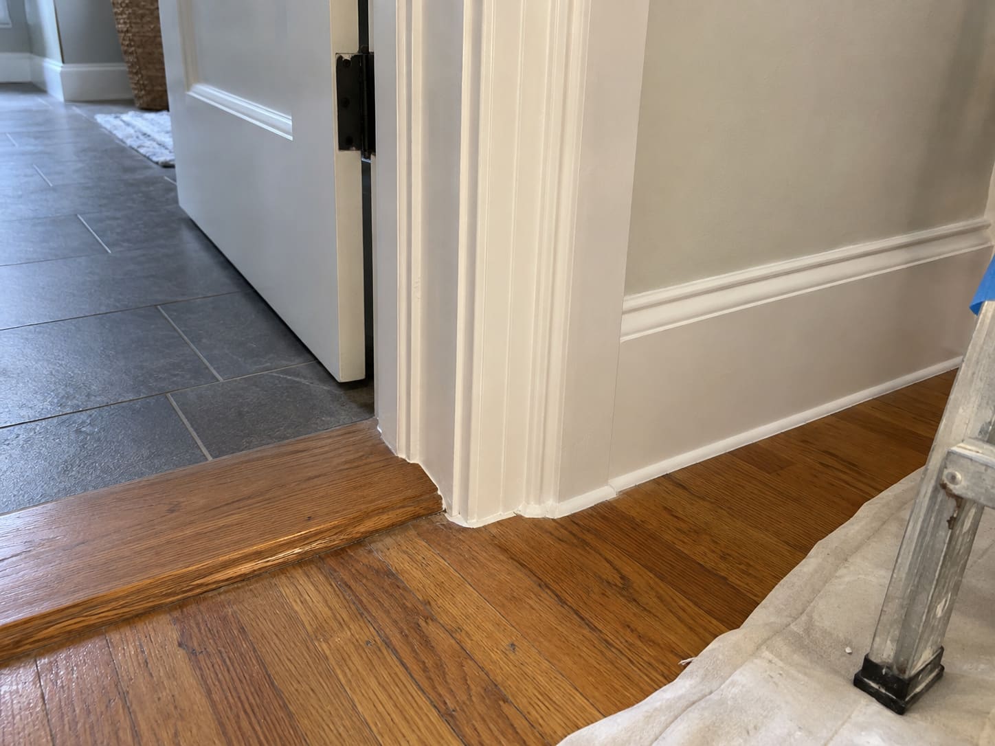A repaired and painted door casing and baseboard corner, with a wood threshold strip at a change in the floor.