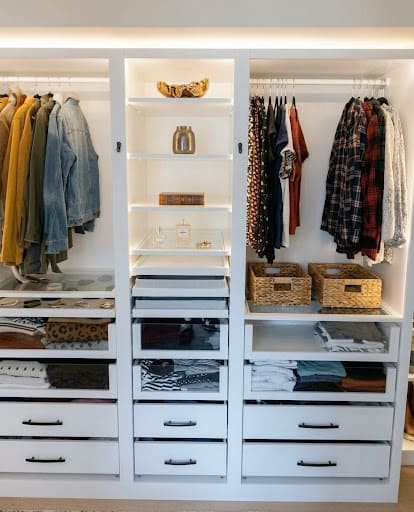 A white built-in closet with warm LED light under the shelves and above the hanging rods.